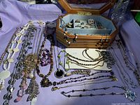 Jewelry box open showing rings, earrings, brooches inside, necklaces and bracelets laid out on surface
