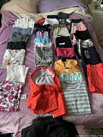 Full view of assorted ladies tops, jackets, tanks, shorts, and capris neatly folded on a bed, showing variety of colors, prints, and styles