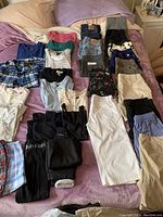 Wide assortment of ladies clothing laid out on bed including jeans, shorts, tops, and tights.
