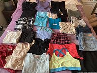 All clothing items laid out on a pink blanket, showing the variety of tops, bottoms, and sleepwear in mostly casual styles.