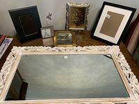 View of all items in the lot arranged on a surface showing the large ornate mirror, two small paintings in decorative frames, and additional frames.