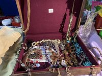 Photo of open box filled with assorted costume necklaces showing mixed bead styles, chains, and pendants.