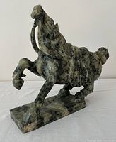 Side view of green and black speckled stone carving of a rearing stallion horse on rectangular base