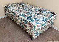 Twin size mattress and box spring with floral pattern on a base metal frame with wheels