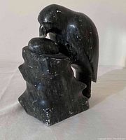 Side and front view of dark polished stone sculpture of a bird feeding its chick.
