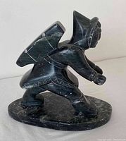 Side view of dark stone Inuit hunter carving showing details of traditional clothing and missing spear.