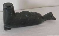 Dark stone seal figurine carving shown from side angle, highlights texture and surface details plus some nicks on body.