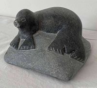 Front angle of dark stone Inuit seal carving resting on base showing detailed front and flipper carvings.