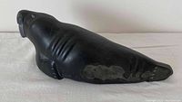 Side view of black soapstone walrus carving on white cloth