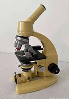 Side angled shot showing the microscope's monocular eyepiece, rotating turret with 3 objective lenses, mechanical stage with slide holder, focusing knobs, and base with condenser.