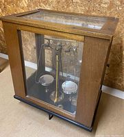 Front and side view of old scientific balance scale inside a wooden case with glass panels