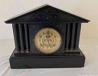 Front view of antique black slate mantel clock with classical design and gold-tone clock face.