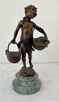 Front view of bronze sculpture showing figure holding two baskets and marble base
