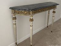 Side angle view of the marble top showing black and white veining, carved gold-accented apron, and cream/gold decorative legs.