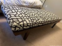 Perspective angle of contemporary cushioned bench showing patterned fabric cover and wooden legs.