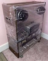 Front view of shrinkwrapped tape deck showing dual reel hubs, VU meters, control knobs