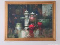 Frontal photo of the framed oil painting showing the still life arrangement with two red apples and various ceramic vessels on a reflective surface.