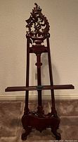 Front view of the wooden tripod easel showing ornate carving, structure, and finish.