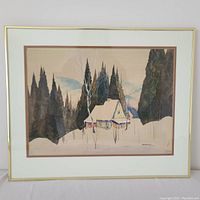 Framed watercolor painting showing snow-covered cottage and forest
