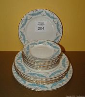 Stack of 16 plates showing 1 large dinner plate at bottom, 6 medium lunch plates, and 9 small side plates on top. Plates feature blue fern design and gold scalloped edges.