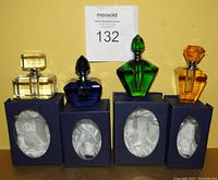 Four colored crystal glass perfume bottles displayed on their respective original navy blue boxes with satin lining inside. Bottles are clear, blue, green, and amber colors with geometric faceted designs and matching stoppers.