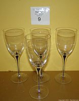Photo of four clear vintage art glass wine glasses arranged together against a yellow background, showing the royal blue teardrop detail in the stems.