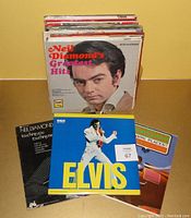 Stack of vinyl LP albums including Neil Diamond's Greatest Hits prominently on top, and Elvis Presley album with a blue background and Elvis in white jumpsuit shown separately in front.