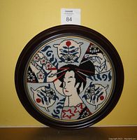 Front view of circular needlepoint artwork featuring Japanese geisha girl in dark wood frame