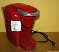Red Keurig single-serve countertop coffee maker shown from front angle with power cord visible.