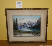 Front view of framed pastel painting depicting Rocky Mountains landscape with pine trees and water body, in gold-toned frame with matting.