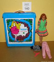 Red head Skipper doll standing next to blue Skipper doll case with clothes and hanger laid out