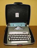Vintage Smith Corona Sterling manual typewriter placed inside its black hard carrying case. Beige typewriter with white round keys and ribbon installed.