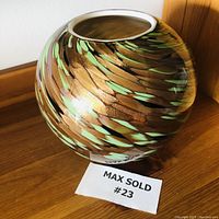 Full side view of the glass bowl showing the gold and green swirl pattern on the rounded surface, sitting on wood surface.