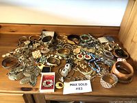 Wide view of the costume jewelry lot spread out on a wooden surface showing multiple bracelets, earrings, rings, and necklaces with various colors and materials.