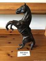Side view of dark brown leather horse figurine rearing on hind legs with detached reins.