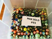 Plastic bin filled with numerous colorful marbles, label showing Max Sold #93