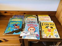 Books displayed on wooden dresser, featuring covers of Raggedy Ann, Mrs. Brisby, Theodore Mouse Goes to Sea, I Can Fly, and others.