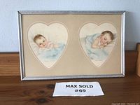 Two heart-shaped baby prints by Charlotte Becker in silver frame, no glass. Prints show a baby awake and a baby sleeping on blue blankets.