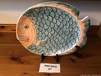 Front view of the vintage fish-shaped ceramic platter showing the detailed scales, pink and green iridescent glaze, and overall shape on a black stand.