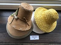 Four vintage ladies straw sun hats displayed on a wooden surface including the tan hat with leaf decoration and the yellow hat