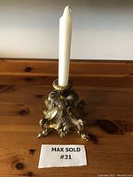 Front view of the ornate heavy brass candle holder with white taper candle on wooden table.