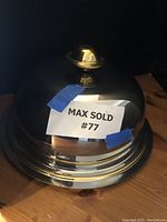 Stainless steel domed serving tray under low lighting, showcasing the shape and gold-tone finial with minor wear.