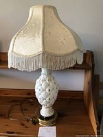 Full view of the vintage milk glass table lamp with Victorian fringe satin brocade shade on wooden surface.