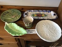 Full view of all serving dishes on wooden surface showing asparagus platter, cabbage leaf plates, lettuce leaf dish, hand-painted tray, and dip container.