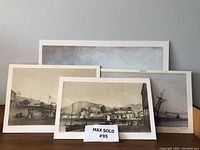 Four monochrome lithograph prints spaced against a grey wall, showing vintage Trinidad scenes.