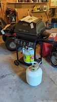 Side view of gril with attached propane tank and second detached propane tank in front, located in garage.