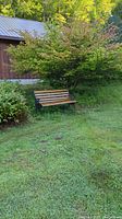 Wood panel bench with metal frame positioned outdoors on grass near shrubbery and wooden building