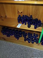 Wide shot of wooden shelves holding many small to medium blue glass bottles and jars arranged in groups by size and shape.