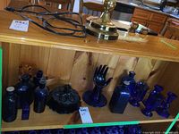 Wide view of shelf displaying the blue glass items including hand sculpture, bottles, candle holders, butter dish and mugs.