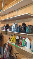Shelved assortment of automotive chemicals on wooden shelves inside garage showing bottles, spray cleaners, and funnels.